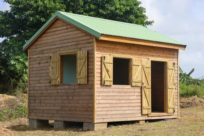 Kaz à Titine en bois naturel, avec volets ouverts et toiture verte